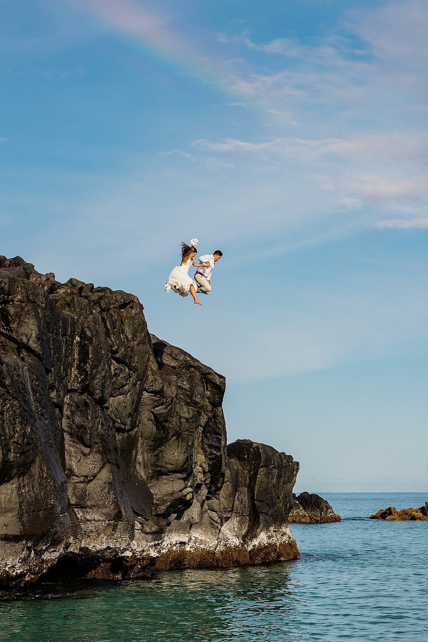 bride and groom jumping off rock into the ocean during Haleiwa elopement