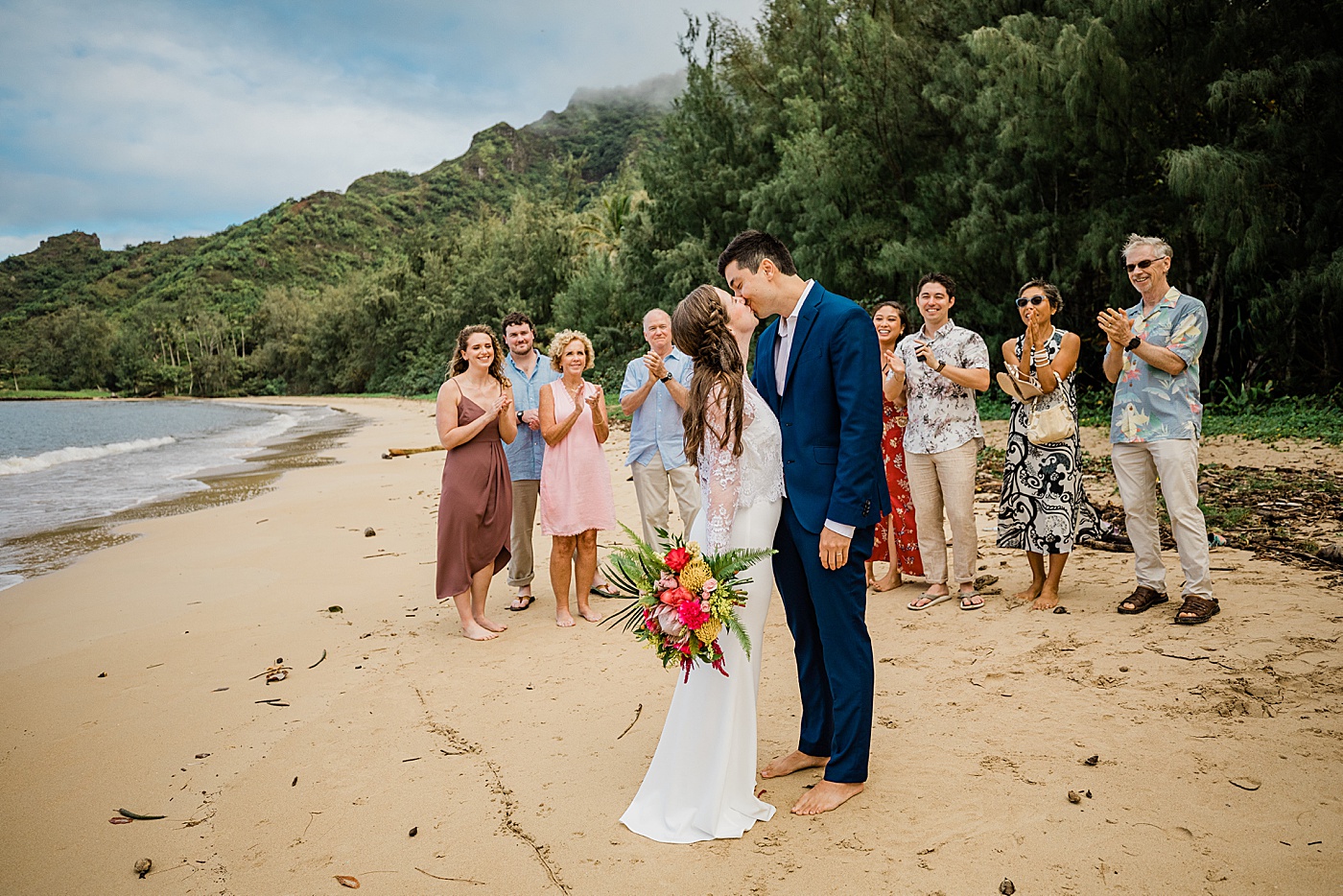 Adventurous Oahu elopement at the beach. Bride and groom kissing with family celebrating
