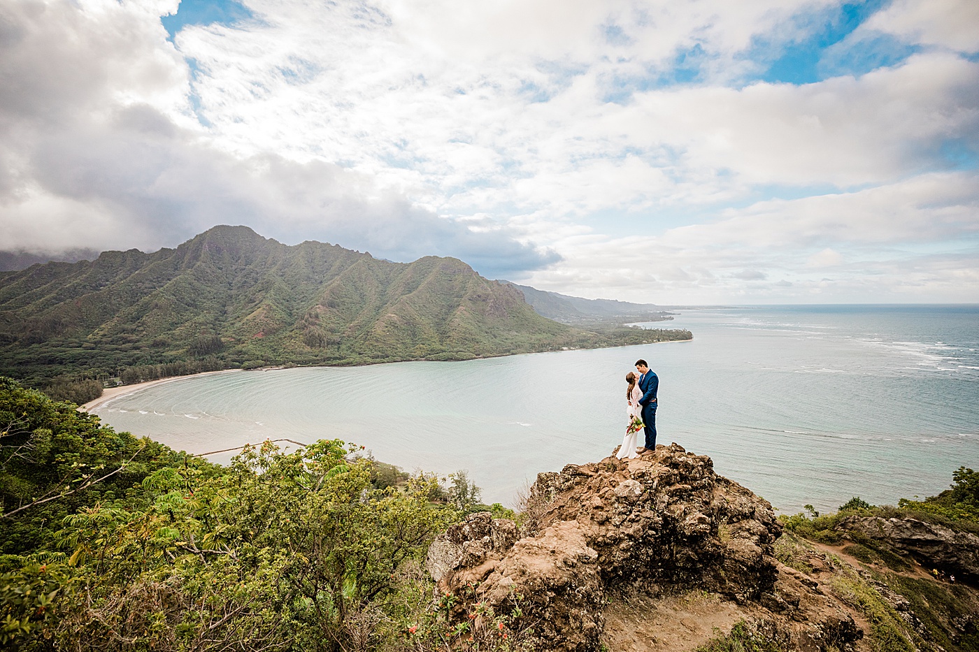 Adventurous Oahu elopement. The bride and groom standing on a cliff kissing in front of the ocean.