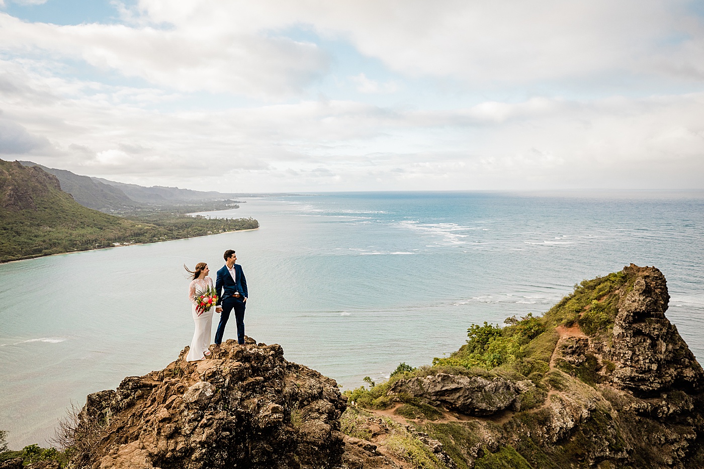 Adventurous Oahu elopement. The bride and groom standing on a cliff in front of the ocean.