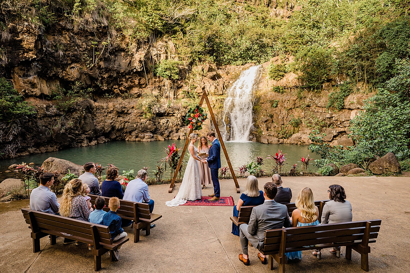 Bride and groom standing in front of family on benches at Waimea Valley wedding.
