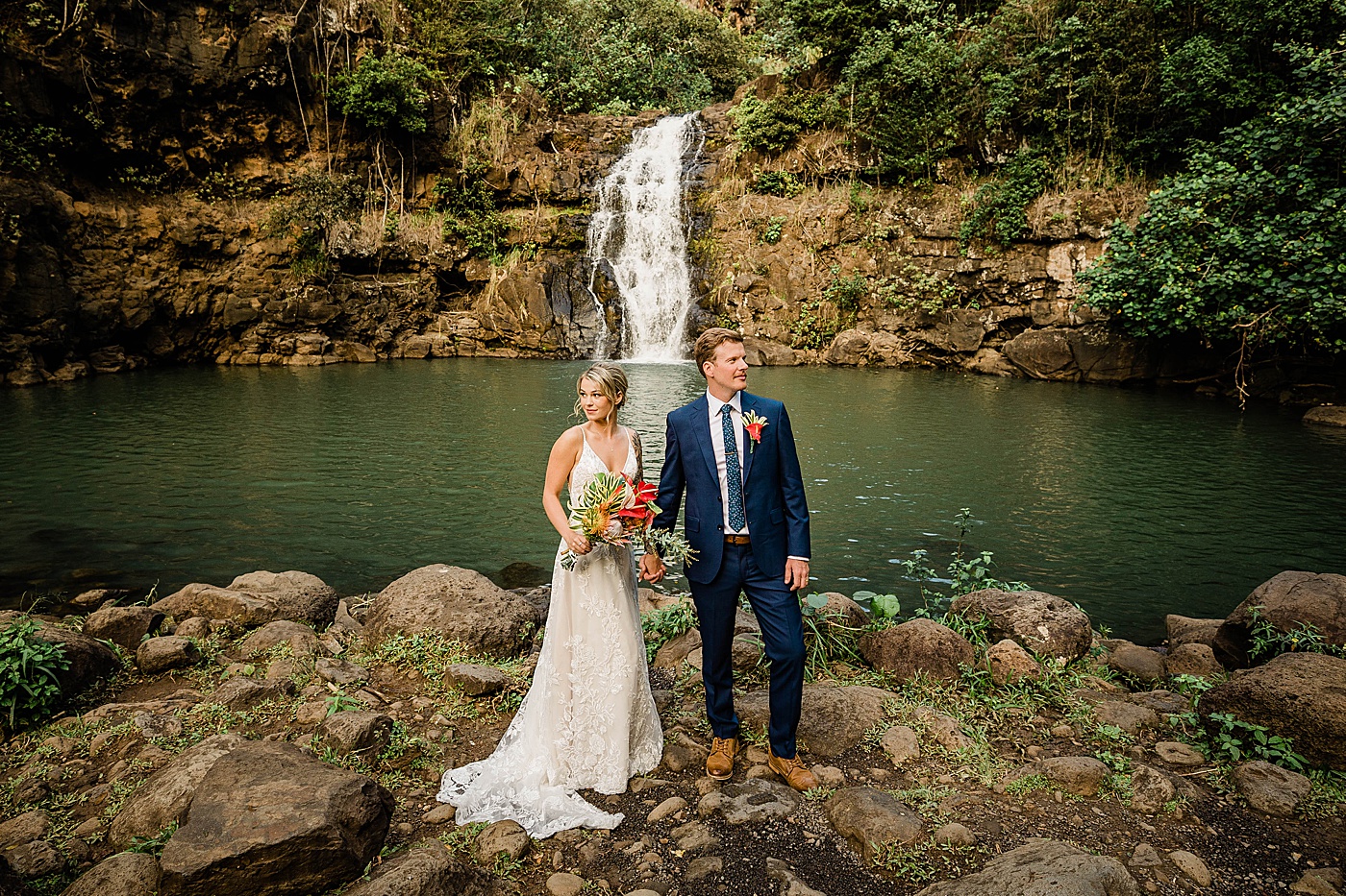 Waimea Valley wedding. Bride and groom holding hands in front of waterfall.