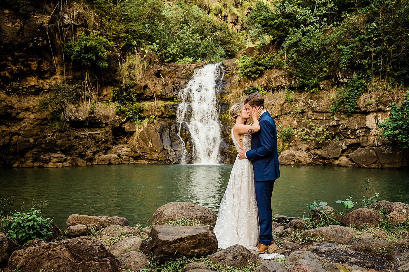 Waimea Valley wedding. Bride and groom kissing in front of waterfall.