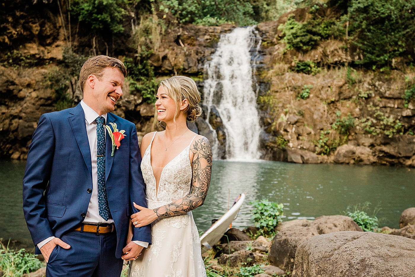 Waimea Valley wedding. Bride and groom holding hands and laughing in front of waterfall.